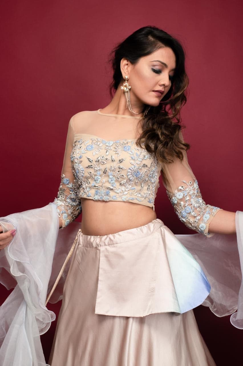 Studio close-up of the peach-to-blue ombre lehenga — nude mesh blouse with silver and pale-blue floral embroidery, organza ruffle sleeves caught mid-twirl.