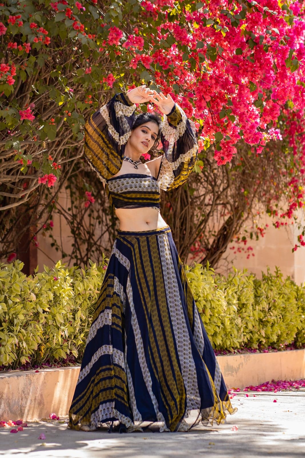 Compact-frame study of the indigo and ochre block-printed lehenga — striped Rajasthani patterning, photographed beneath cascading bougainvillea.