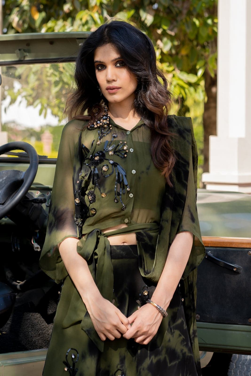 Close portrait of the olive green sequined sharara — three-dimensional bead-and-sequin embroidery in detail, photographed against the vintage Jeep door.