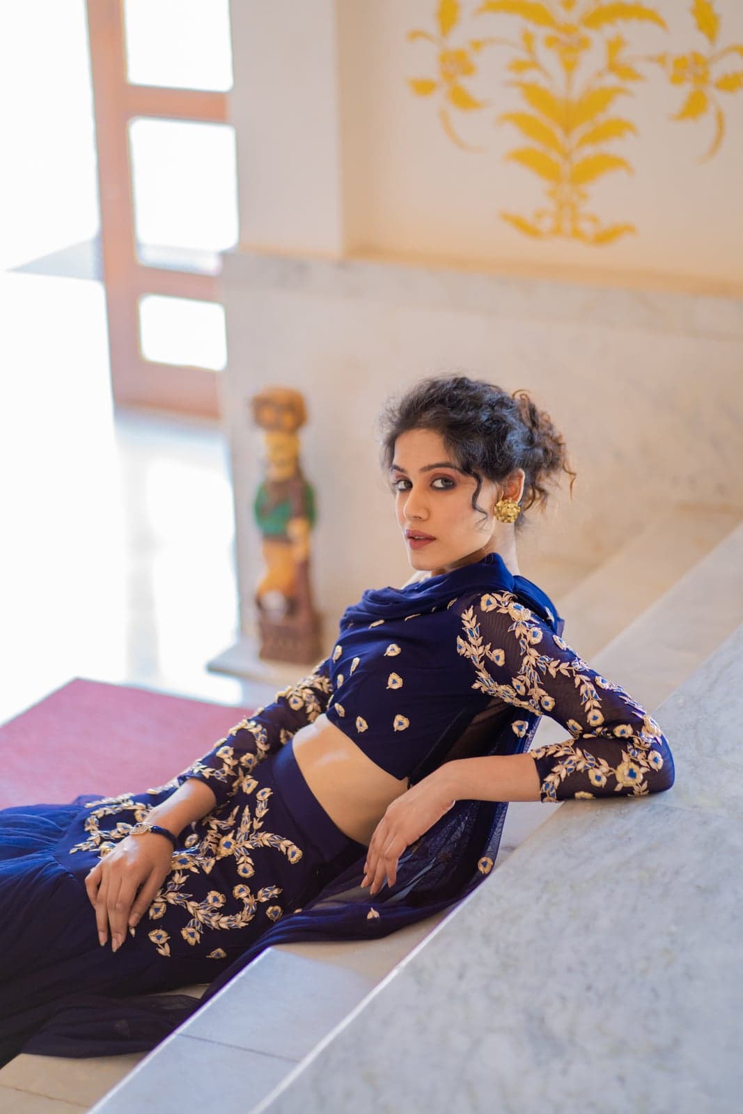Reclining detail of the sapphire blue lehenga bodice — gold zardozi floral embroidery on midnight tulle, oxidised studs, photographed against a marble plinth.