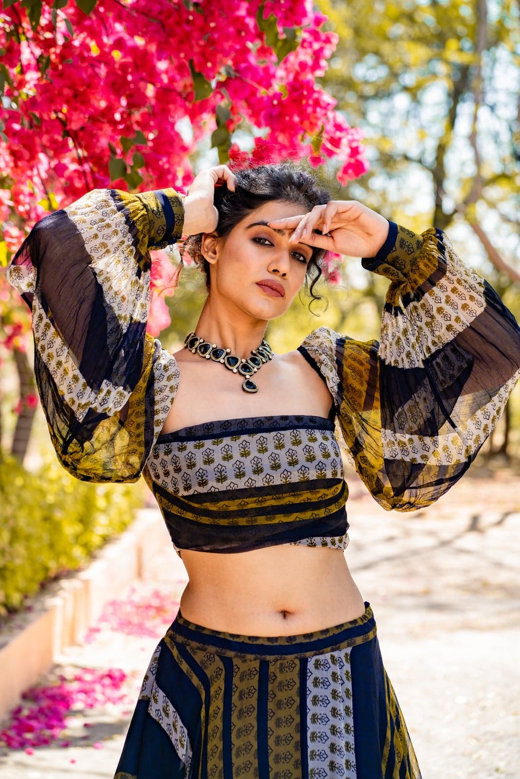 Bougainvillea-framed close-up of the indigo and ochre block-printed lehenga — oxidised silver collar in focus.