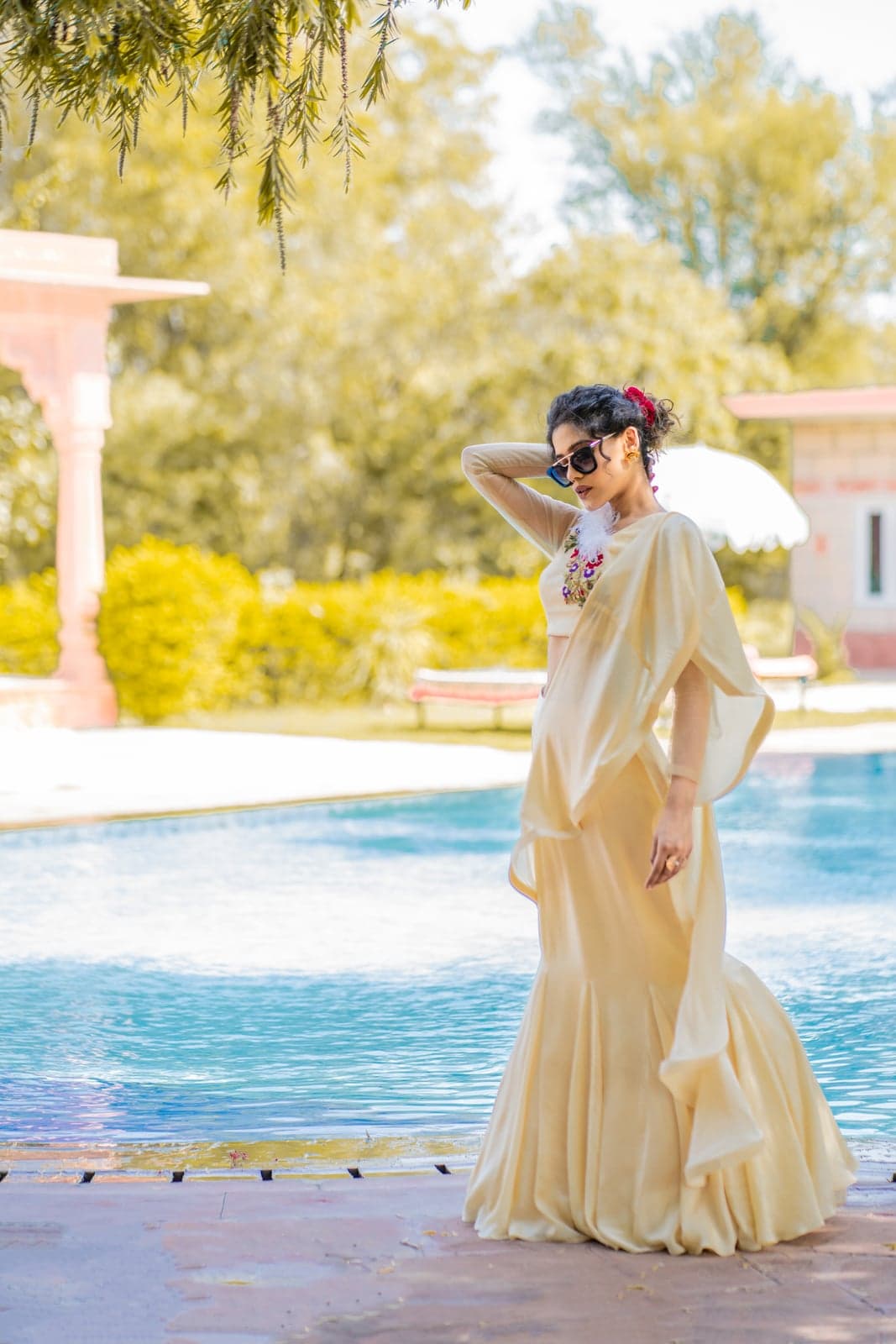 Champagne mermaid lehenga in motion — sheer cape catching afternoon light across the pool at a Jaipur villa.