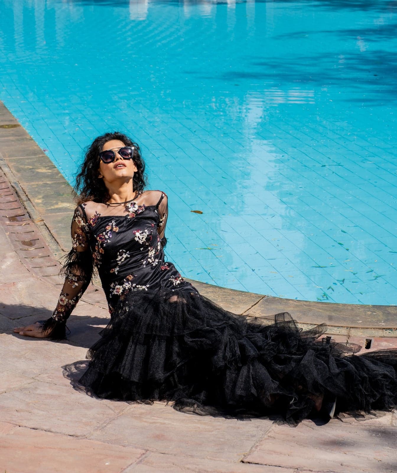 Black floral gown with tulle ruffled train — reclining study on warm sandstone beside a Jaipur villa pool.