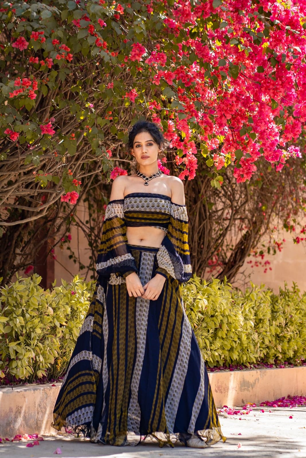 Indigo and ochre block-printed lehenga — bougainvillea-framed portrait, layered striped panels of the skirt in detail.