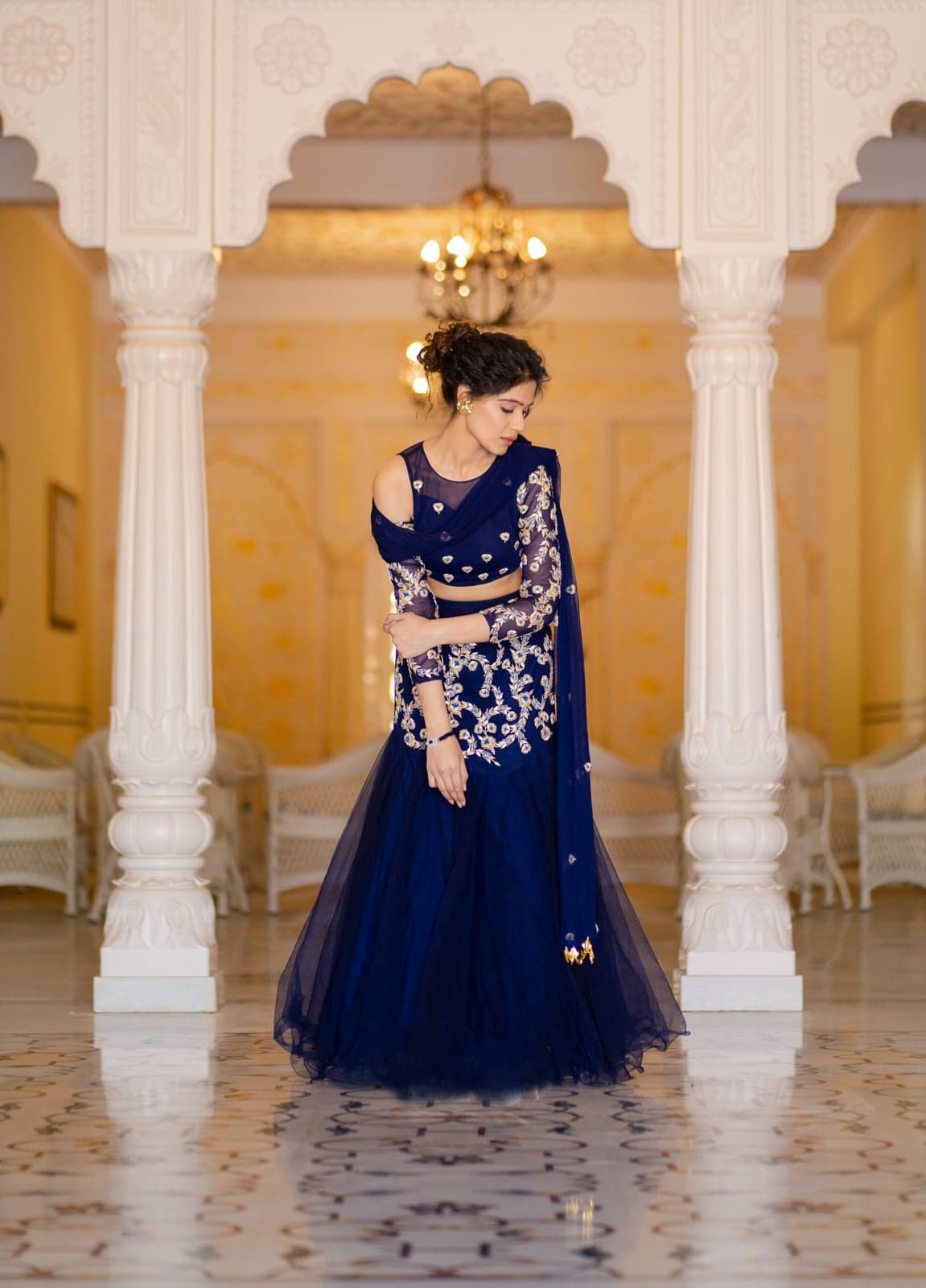 Sapphire blue mermaid lehenga — studio-lit silhouette beneath the cusped arches of a Jaipur palace hall.