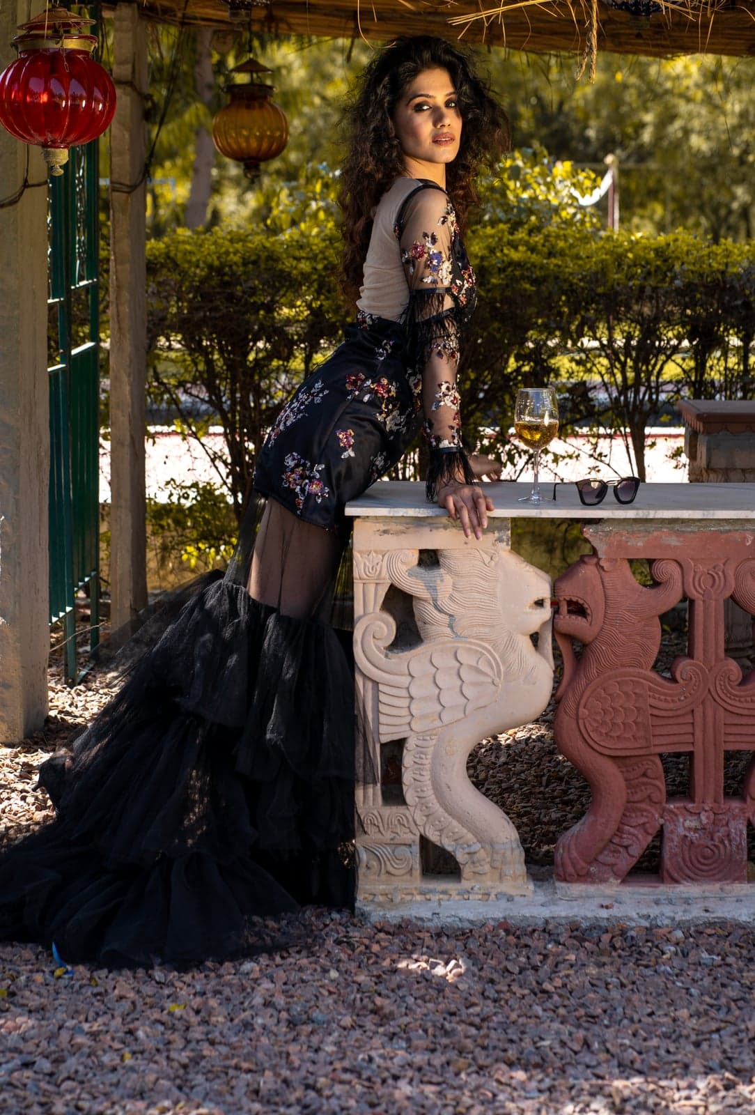 Black floral-embroidered gown — reclining pose against carved sandstone railings, tulle train cascading onto the gravel.