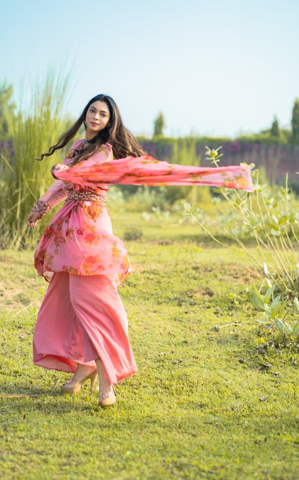 Pink rose-print chiffon palazzo set in motion — mid-twirl with the sheer dupatta arcing behind.