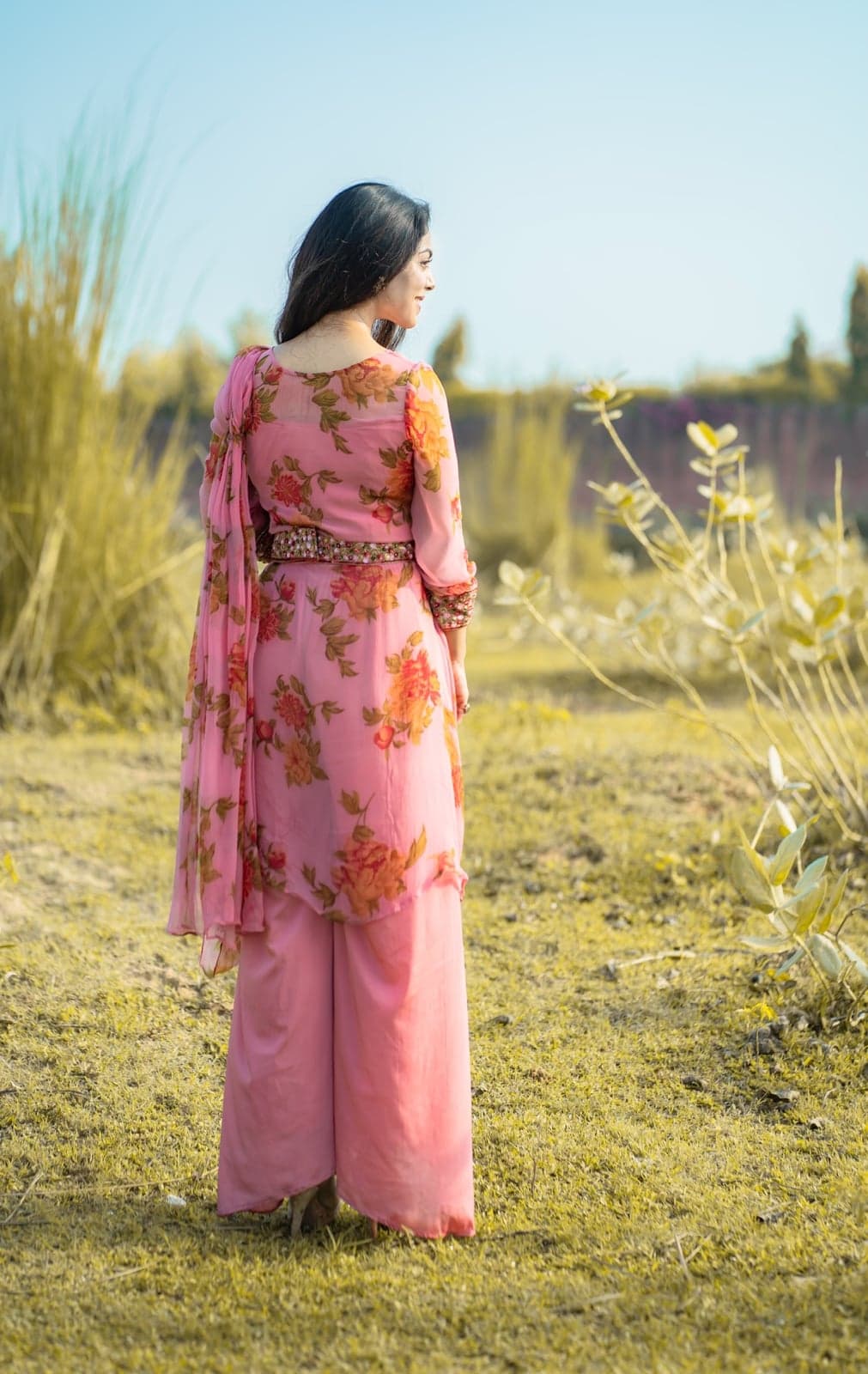 Pink chiffon kurta with rose-print sleeves — back-view portrait in pampas grass.