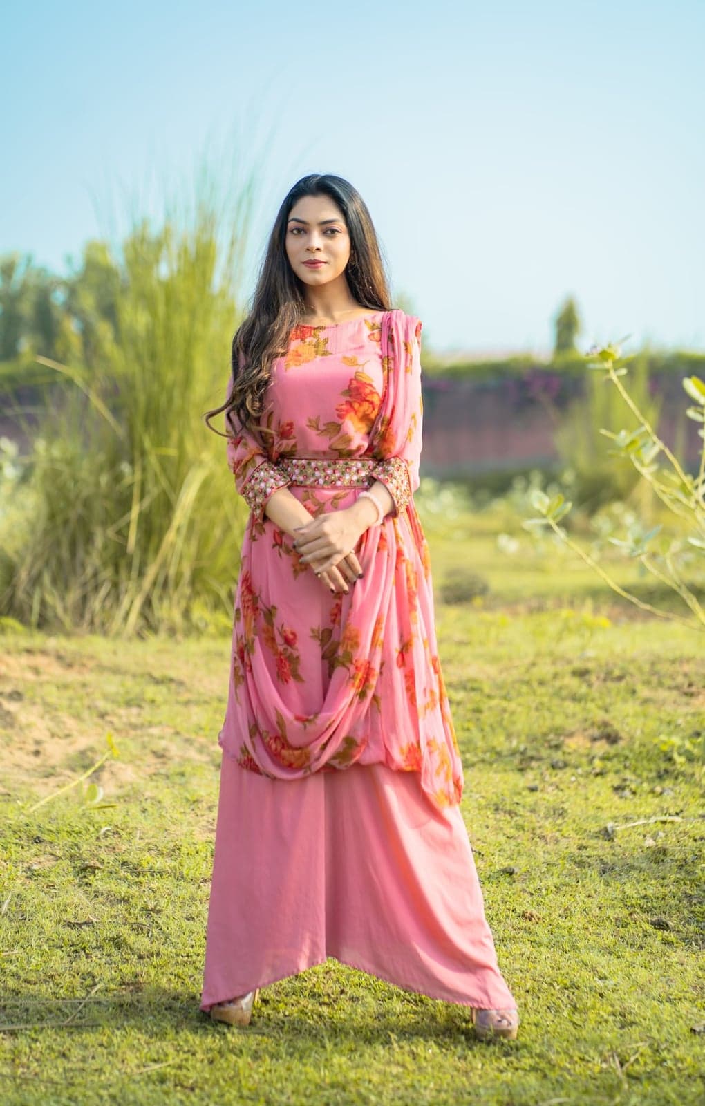 Pink chiffon set with rose-print sleeves and embellished belt — full-length portrait facing the camera.