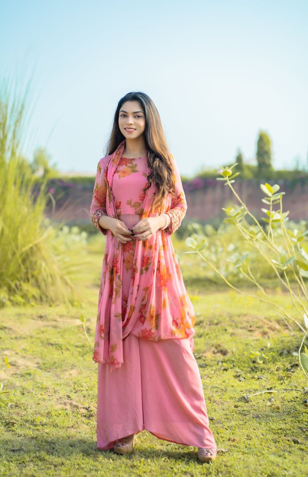 Pink chiffon palazzo set — close studio-light portrait with rose-print sleeves and pearl-and-coral necklace styling.