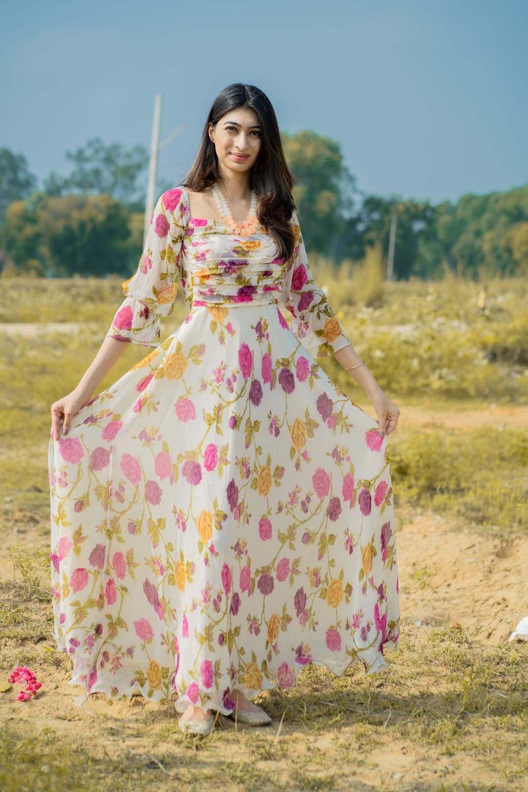 Cream berry-print lehenga on temple steps — pink chiffon dupatta draped along the side, sandstone tier stairs in view.