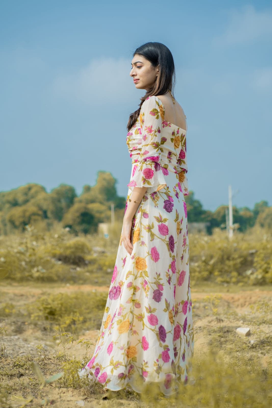 Ivory rose-print maxi — back-side portrait, ruched bodice with the print cascading down to the hem.