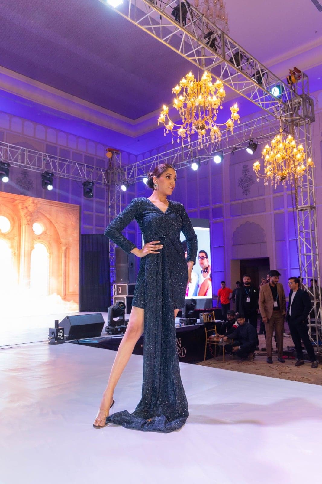 Black sequin sheath with a sleeve-cape — fluid hem trailing the floor, photographed mid-runway under spotlights.