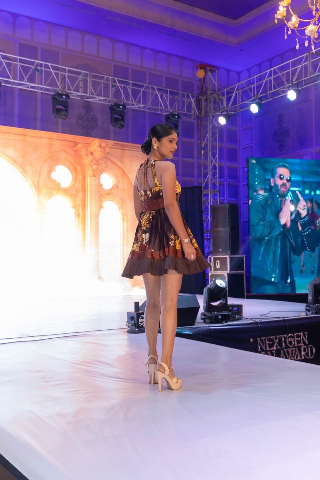 Black floral-embroidered mini dress with a tulle ruffle mermaid hem — close-frame runway portrait beneath spotlights.