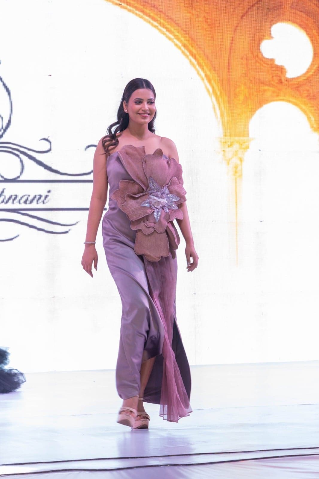 Black lace-trimmed blazer over sheer black lace flared trousers — runway-end portrait flanked by champagne and mauve floral gowns.