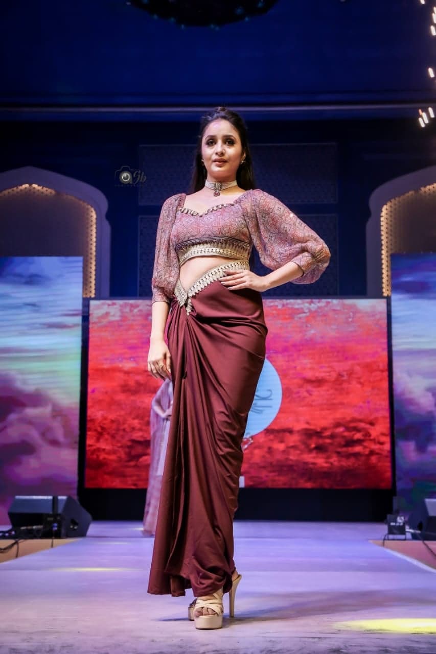Maroon draped saree-skirt with a peach-printed sheer balloon-sleeve crop and an embellished waist — runway walk past a model in patterned crop.