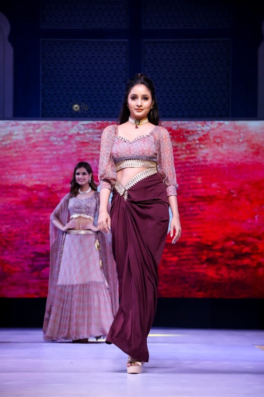 Maroon draped saree-skirt with peach-printed embellished crop and balloon sleeves — solo runway walk with another model in the background.