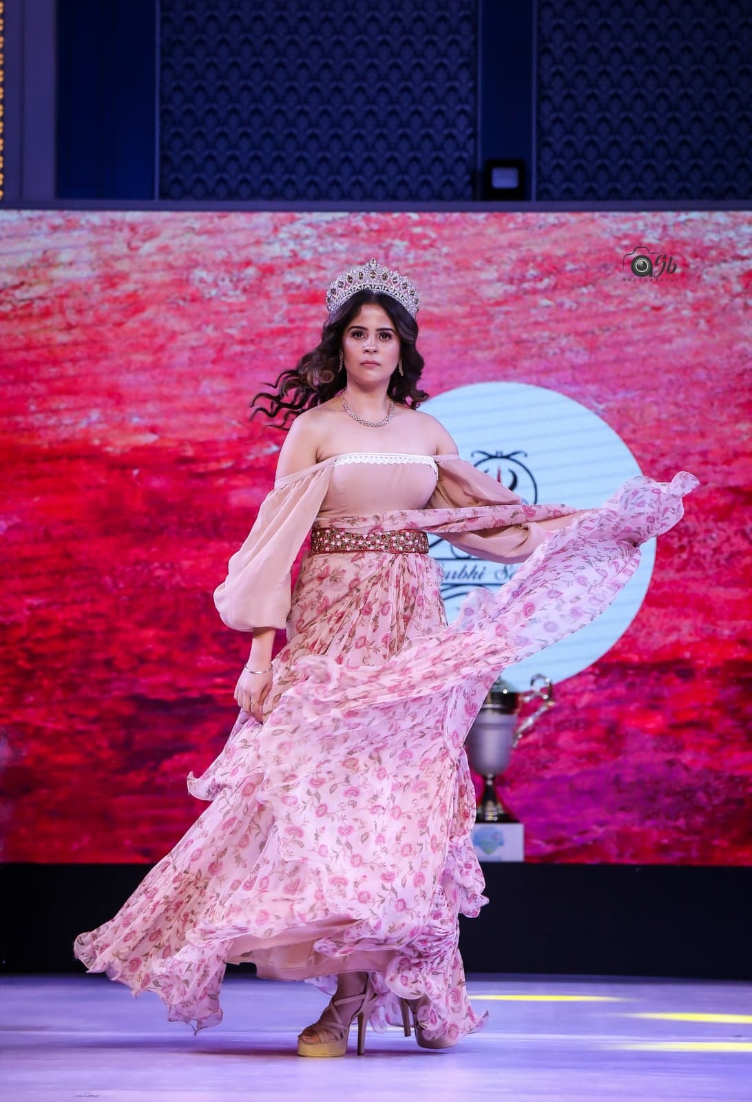 Blush peach floral-rose-print maxi — pirouette mid-runway, ruffle skirt opening out beneath a sparkling crown.