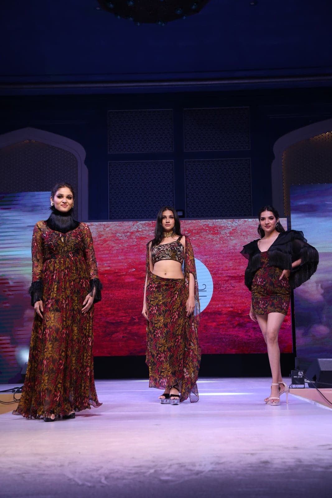 Two-model runway portrait — embellished sequinned emerald-green jacket and palazzo set beside a forest-green tiered embroidered lehenga.