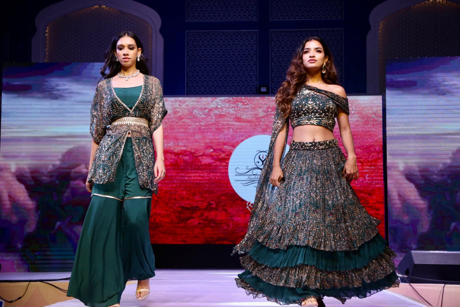 Forest green embroidered lehenga with an off-shoulder embellished bodice and tiered hem — paired with a sequinned green-and-gold jacket in the two-model runway portrait.