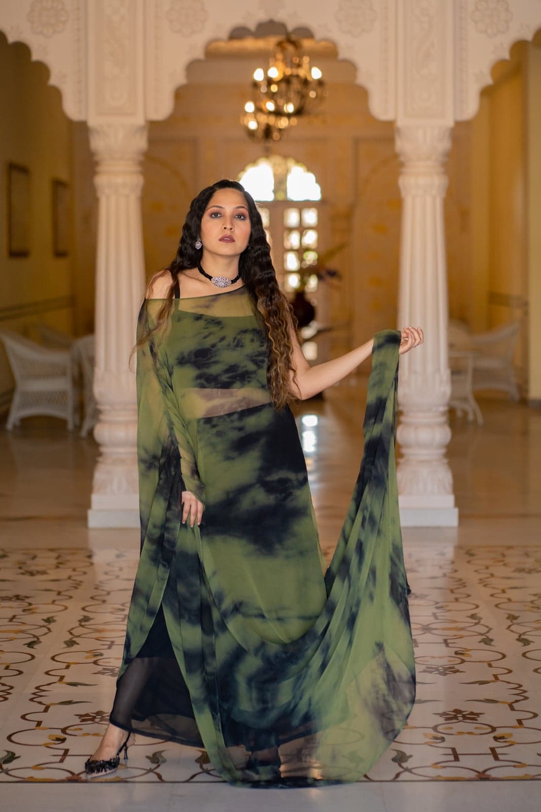 Olive and black tie-dye chiffon kaftan-style sharara with sheer panels and an oxidised silver choker — photographed under the arches of a Jaipur palace hall.