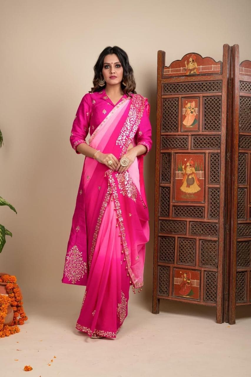 Fuchsia pink saree with an ombre pink palla and gota patti motifs in gold — silk full-sleeve blouse, photographed beside a Rajasthani hand-painted screen.