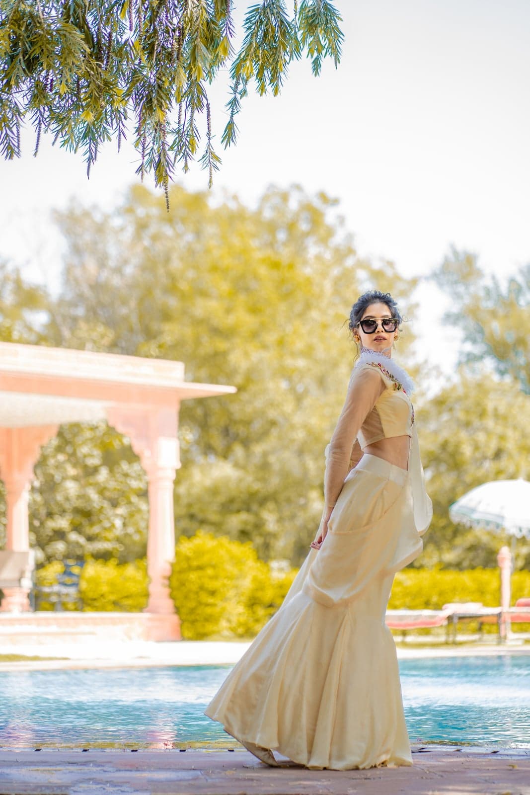 Champagne gold mermaid lehenga with a sheer cape and feathered neckline — fluted satin hem, photographed at the poolside of a Jaipur villa.