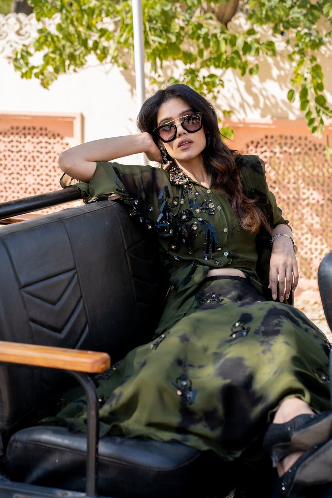 Olive green sharara with hand-set sequin and bead embroidery on the bodice, paired with a black-and-green dyed drape skirt — photographed against the jaali screens of a Jaipur courtyard.