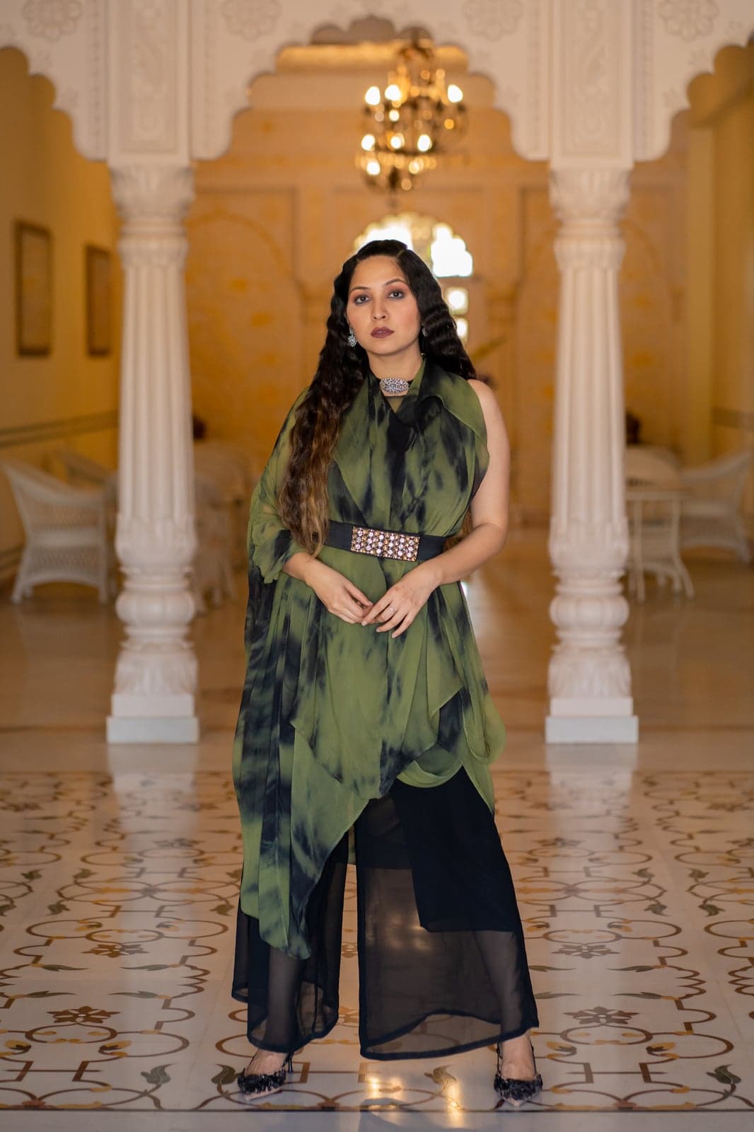 Olive green chiffon belted drape gown — abstract dark-wash kaftan layered over straight-leg trousers, photographed in a Jaipur palace hall.