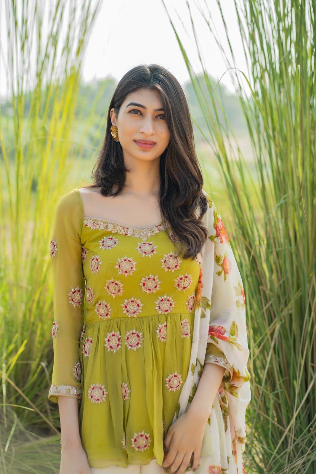 Lime green peplum tunic with circular hand-set bead motifs over a floral printed wide-leg pant — close portrait in a sunlit field of pampas grass.